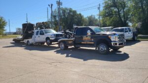A black tow truck from Terry's Auto Service and Towing, LLC, towing a pickup truck with a trailer of pipes in Springfield, MO.
