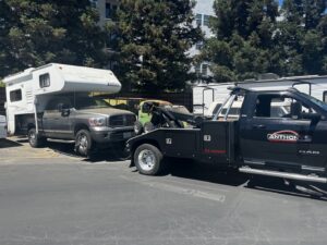 A black tow truck from Anthony's Towing & Transportation towing a large pickup truck with a camper shell in Yuba City, CA.