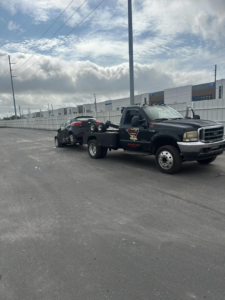 A black No Limit Towing truck actively towing a red car in a parking lot in Orlando, FL.