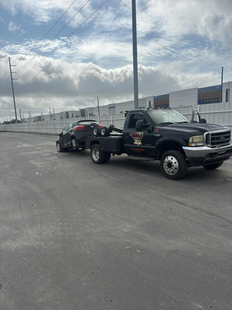 A black No Limit Towing truck actively towing a red car in a parking lot in Orlando, FL.