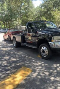 A black No Limit Towing truck actively towing a red car from a parking lot in Orlando, FL.