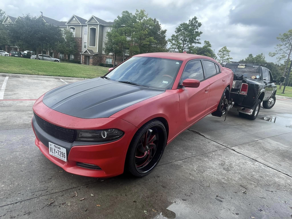 A black tow truck from Houston Towing actively towing a red Dodge Charger with a wheel-lift in Houston, TX.