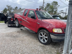 A black tow truck from Houston Towing actively towing a red Ford F-150 pickup truck with a wheel-lift in Houston, TX.