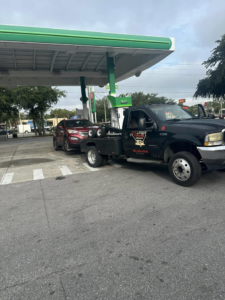A black No Limit Towing truck actively towing a red SUV from a gas station in Orlando, FL.