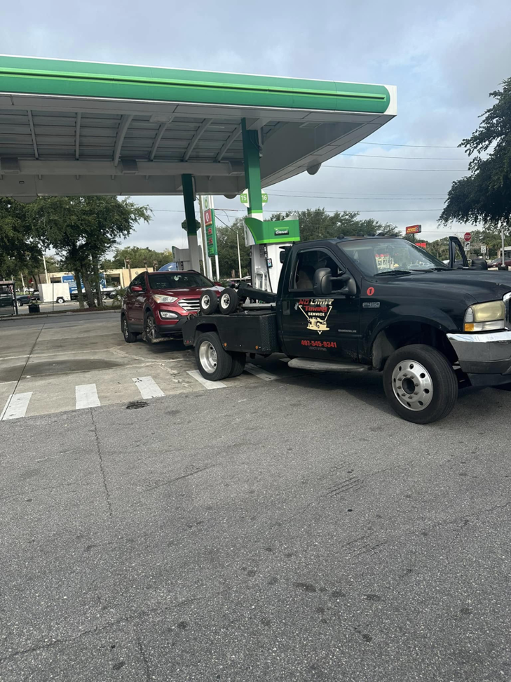 A black No Limit Towing truck actively towing a red SUV from a gas station in Orlando, FL.