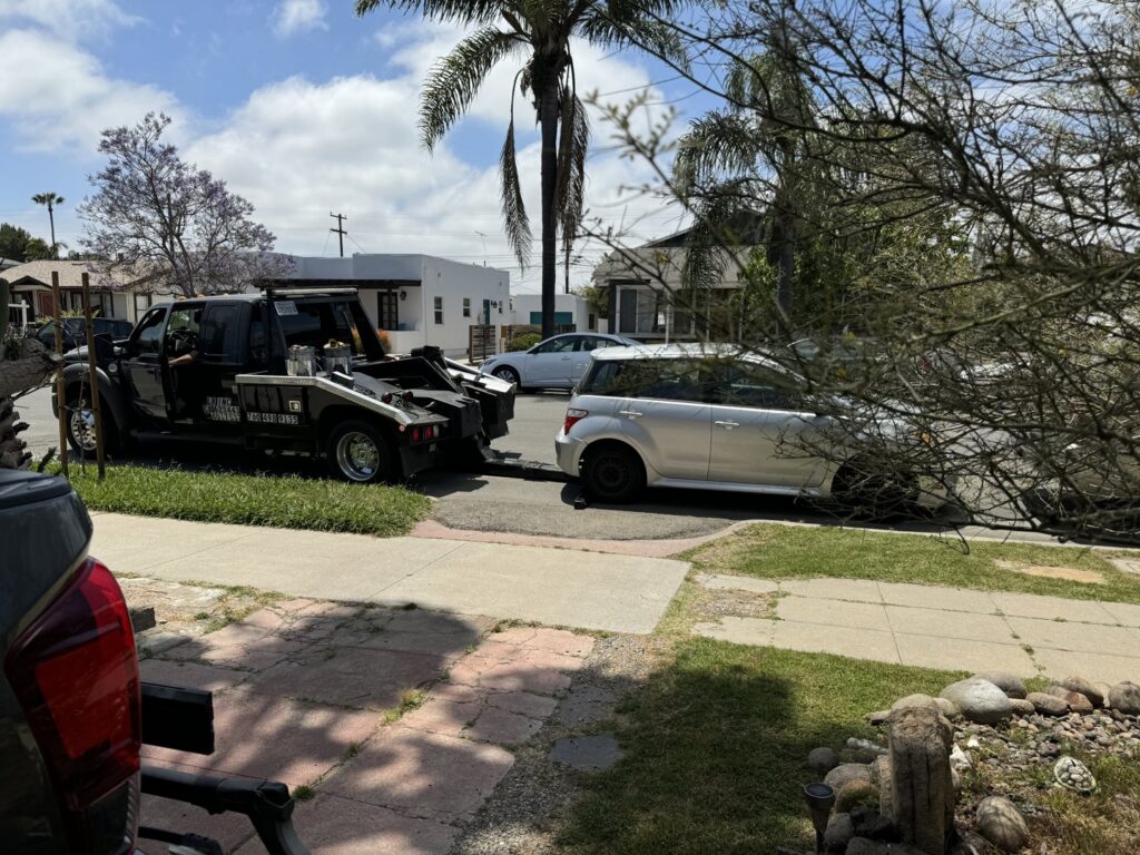 A black tow truck from All Roadside Towing San Diego, CA, using a wheel-lift to tow a silver car.