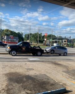 A black No Limit Towing truck actively towing a silver car on a busy street in Orlando, FL.