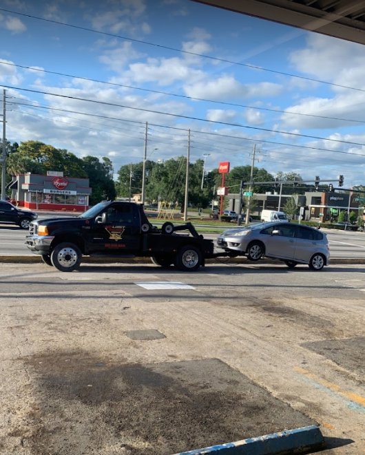 A black No Limit Towing truck actively towing a silver car on a busy street in Orlando, FL.