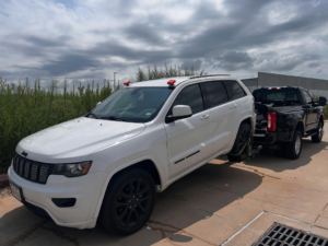 A black tow truck from Houston Towing actively towing a white Jeep Grand Cherokee with a wheel-lift in Houston, TX.