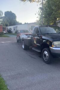 A black No Limit Towing truck actively towing a white SUV on a residential street in Orlando, FL.