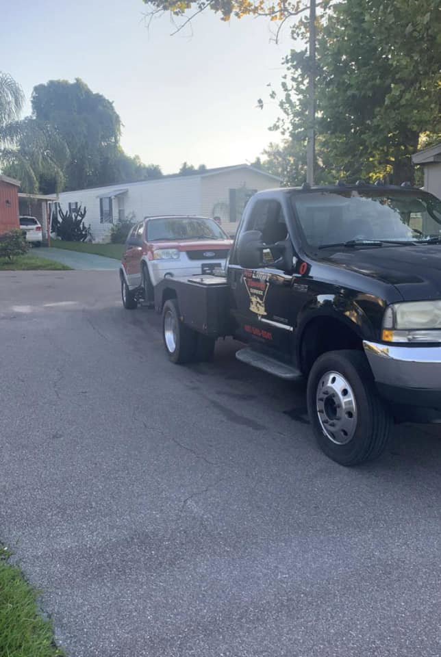 A black No Limit Towing truck actively towing a white SUV on a residential street in Orlando, FL.