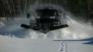 A black truck with a snow plow actively clearing a snow-covered area for American Snow Plowing Services in Rockville, MD.