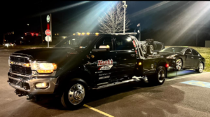 A black wrecker tow truck from Hank's Auto Service towing a dark sedan at night in Bethlehem, PA.