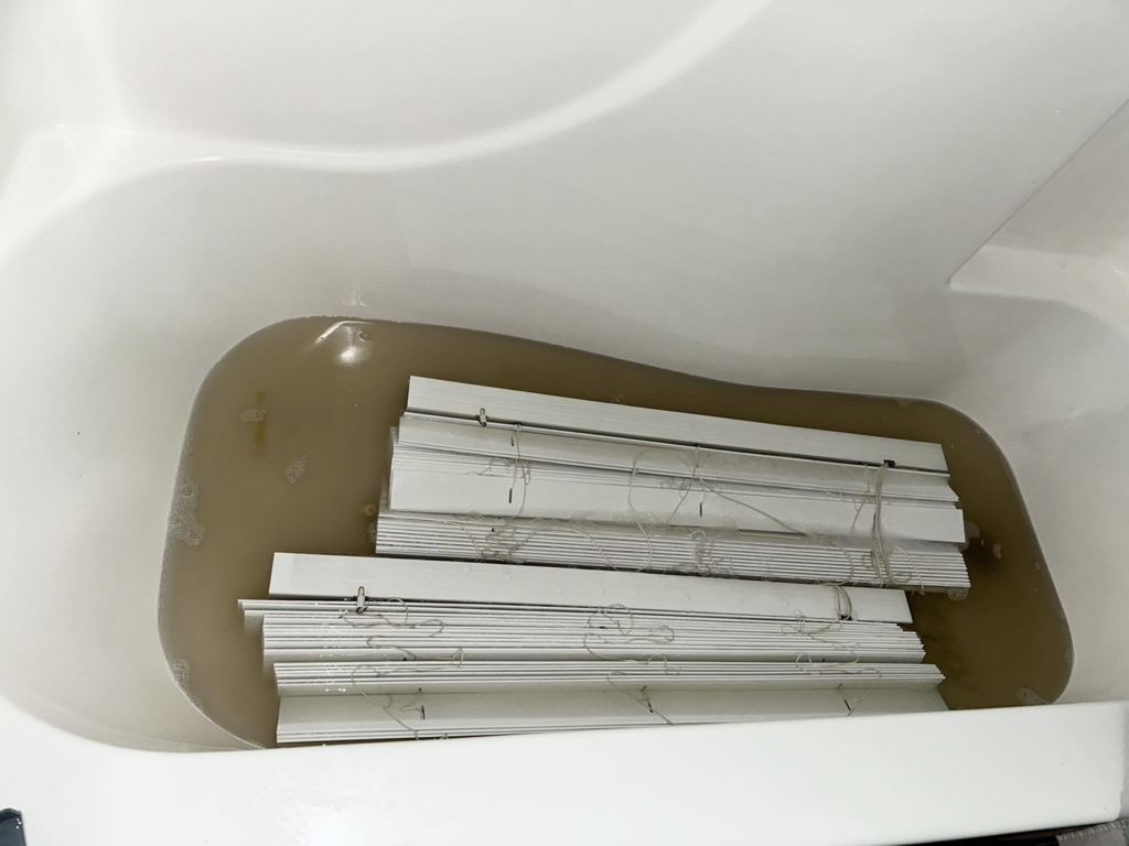 White window blinds soaking in a bathtub during a deep cleaning service by Jaybug's Services LLC in Pontotoc, MS