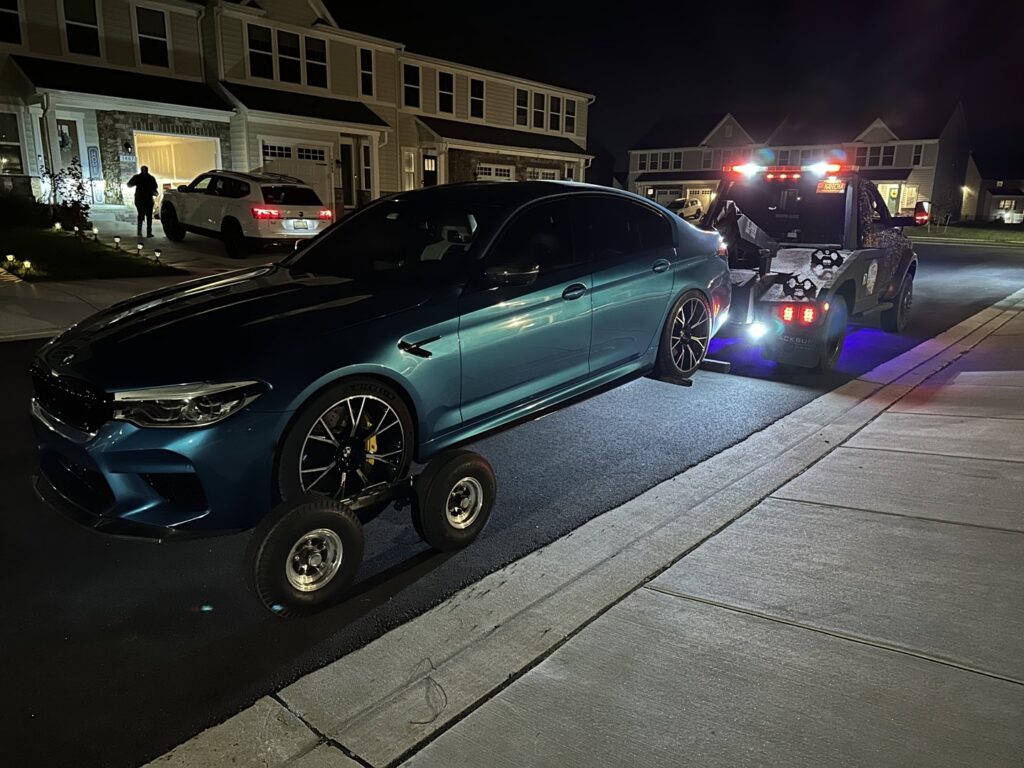 A blue BMW being towed with dollies at night by Nacho Transports llc in Middletown, DE.