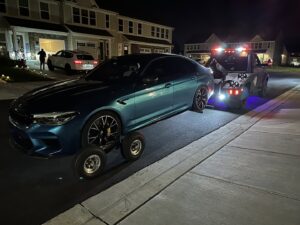 A blue BMW being towed with dollies at night by Nacho Transports llc in Middletown, DE.