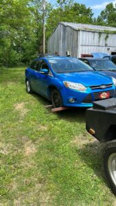 A blue car being loaded onto a flatbed tow truck with wooden blocks by Tow Truck Company in Johnson City, TN.