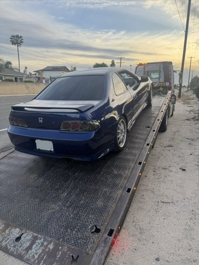 A blue car being towed on a flatbed tow truck by Affordable Towing LLC in Anaheim, CA, at sunset.