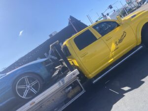 A blue car being transported on a yellow flatbed tow truck by Ledesma's Towing in San Diego, CA.