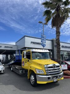 A blue car is loaded onto a flatbed tow truck by S&F Towing outside a dealership in Oakland, CA.