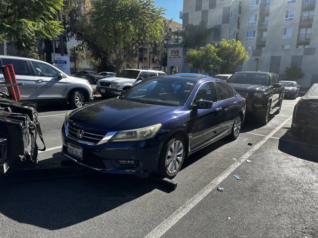 A blue car being towed by a wheel-lift tow truck in a parking lot by Dixon's Towing & Roadside Assistance in Dallas, TX.
