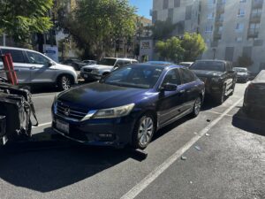 A blue car being towed by a wheel-lift tow truck in a parking lot by Dixon's Towing & Roadside Assistance in Dallas, TX.
