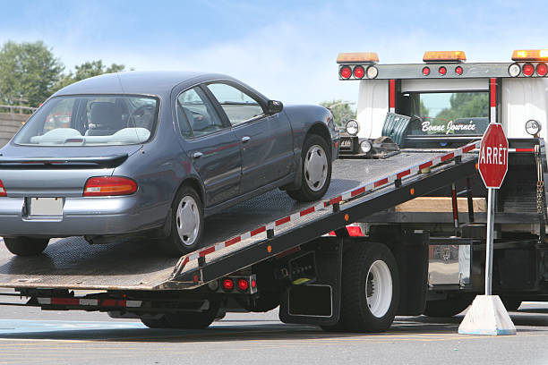 A blue sedan being transported on a flatbed tow truck by Jensen Towing in Kenosha, WI.