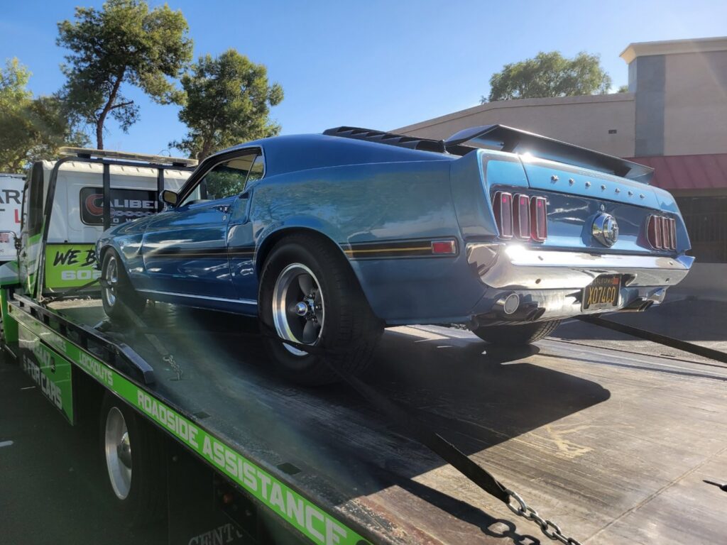 A blue classic Ford Mustang being transported on a flatbed tow truck by Caliber Towing in Phoenix, AZ.