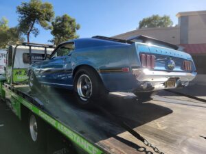 A blue classic Ford Mustang being transported on a flatbed tow truck by Caliber Towing in Phoenix, AZ.