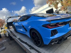 A blue Corvette C8 sports car being transported on a flatbed tow truck by California Auto House in Sacramento, CA.