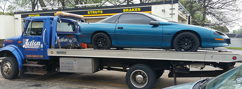 A blue flatbed tow truck from Action Towing transporting a blue sports car in Rockford, IL.
