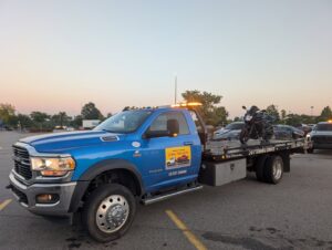 A blue flatbed tow truck from Snoork Towing transporting a black motorcycle in a parking lot in Charlotte, NC.