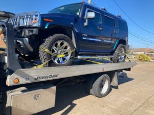 TJ Towing LLC flatbed truck towing a large blue Hummer H2 with custom wheels in New Orleans, LA.