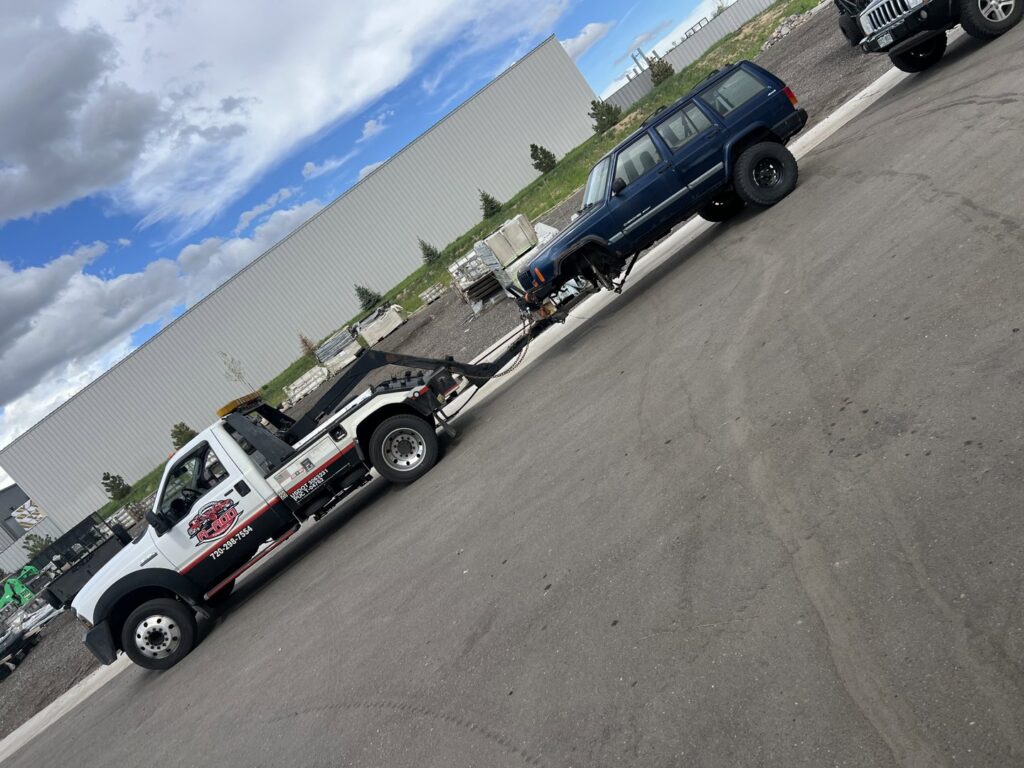 A blue Jeep being towed by a wheel-lift tow truck from A-ROD Towing in Denver, CO.