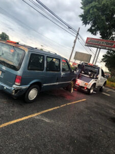 A blue minivan being towed by a J & G Towing, LLC truck, providing roadside assistance in Greensboro, NC.