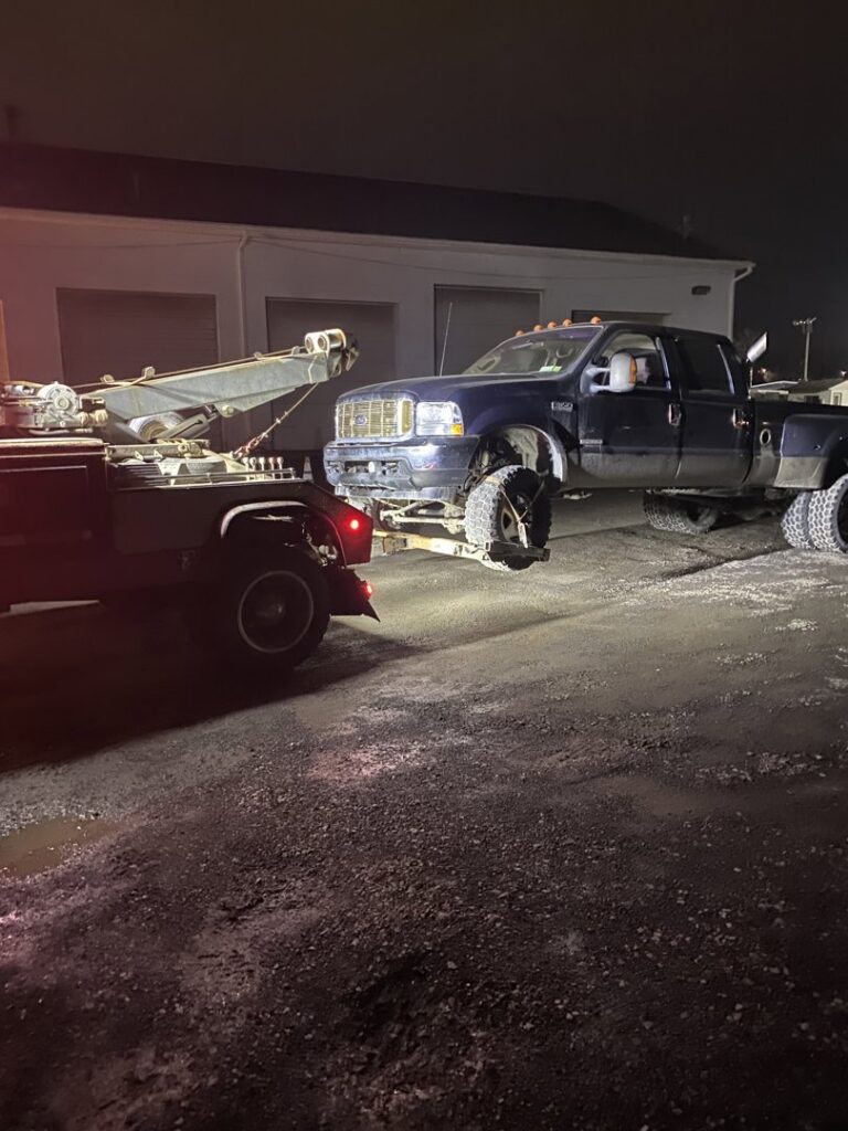 A blue pickup truck being towed by RonniesTowing&Recovery at night in Bryan, TX