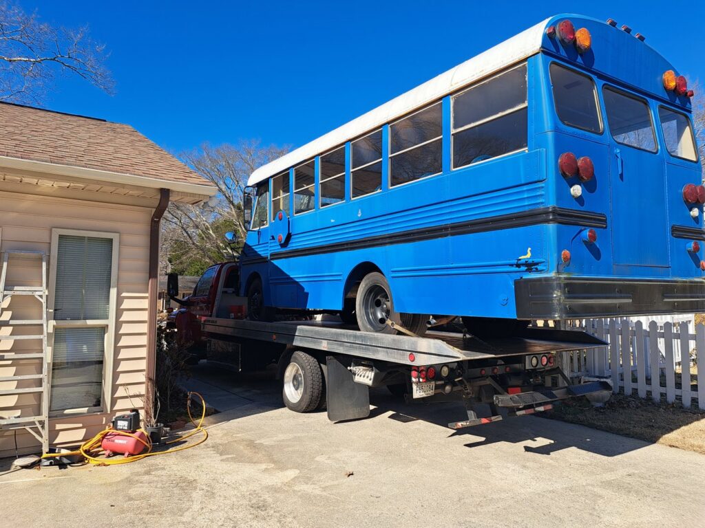 A blue school bus being loaded onto a flatbed tow truck for transport by Acme Towing Services in Greenville, SC.
