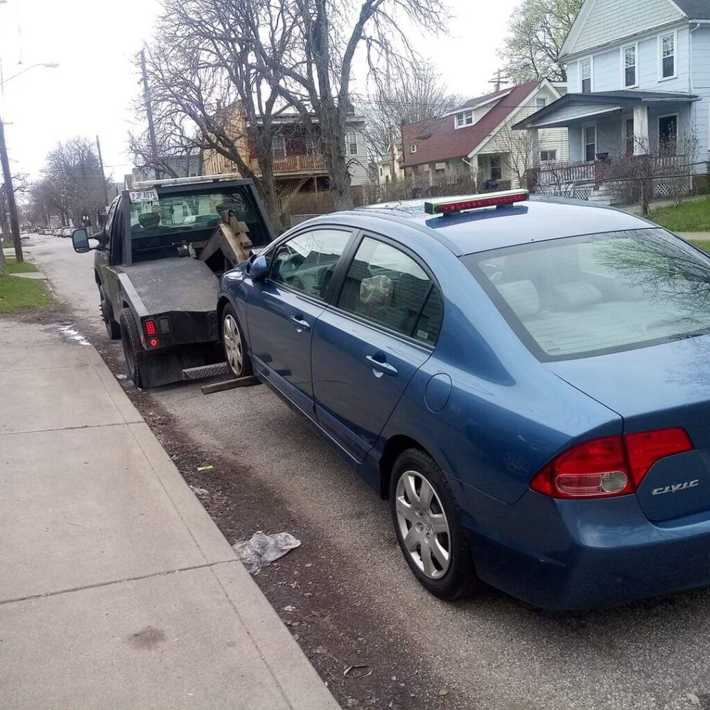 A blue sedan being towed by a wrecker-style tow truck from Quiñones Towing in Cleveland, OH.