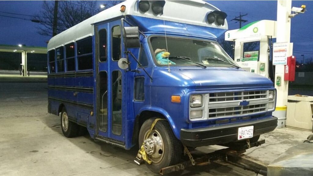 A blue short bus being towed by Whitelock Towing in Baltimore, MD, from a gas station.