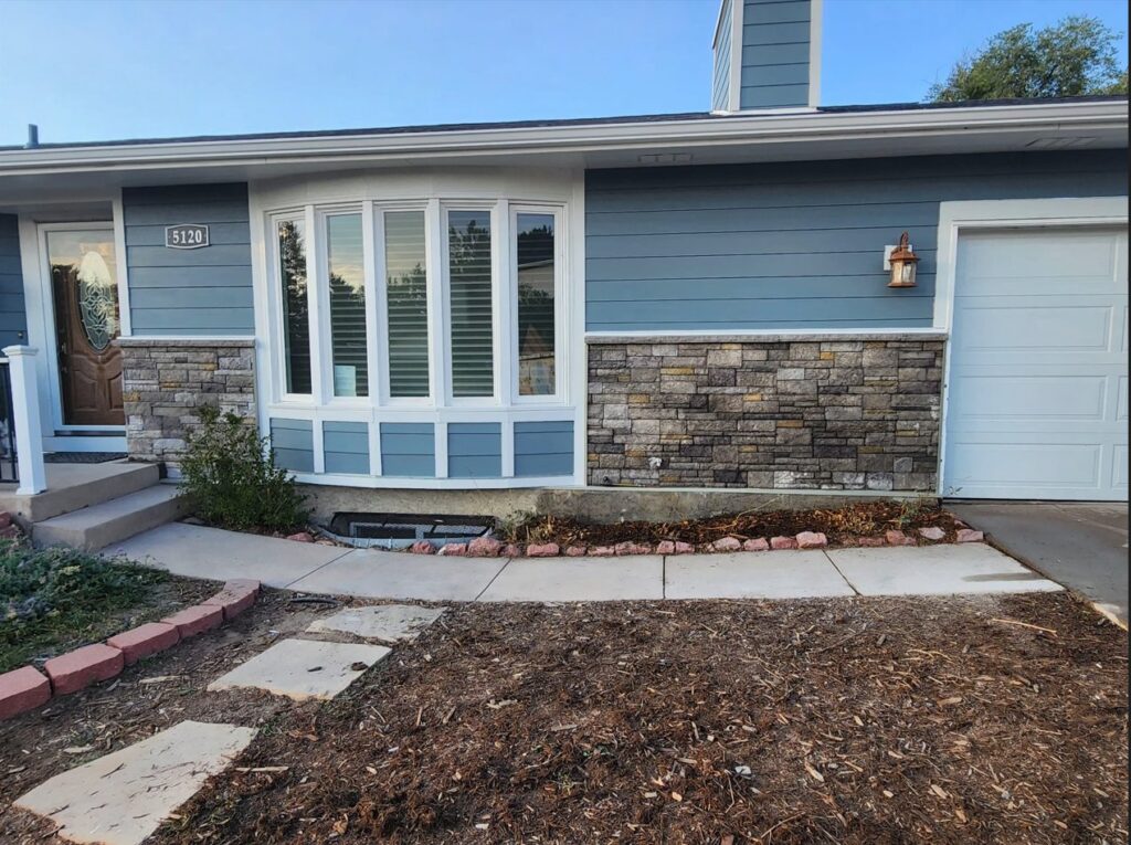 Front of a house with new blue siding and decorative stone veneer, installed by EZ General Construction in Colorado Springs, CO.