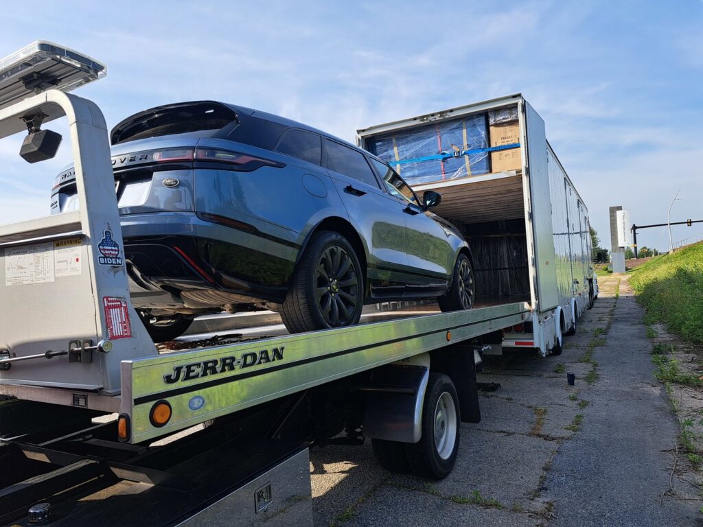 A blue SUV being transported on a flatbed tow truck next to a large trailer by Acme Towing Services in Greenville, SC.
