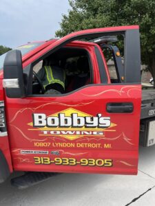 Side view of a red tow truck with Bobby's TCB Towing branding and contact information in Detroit, MI