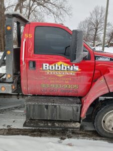 Side view of a red tow truck from Bobby's TCB Towing, covered in ice and snow in Detroit, MI