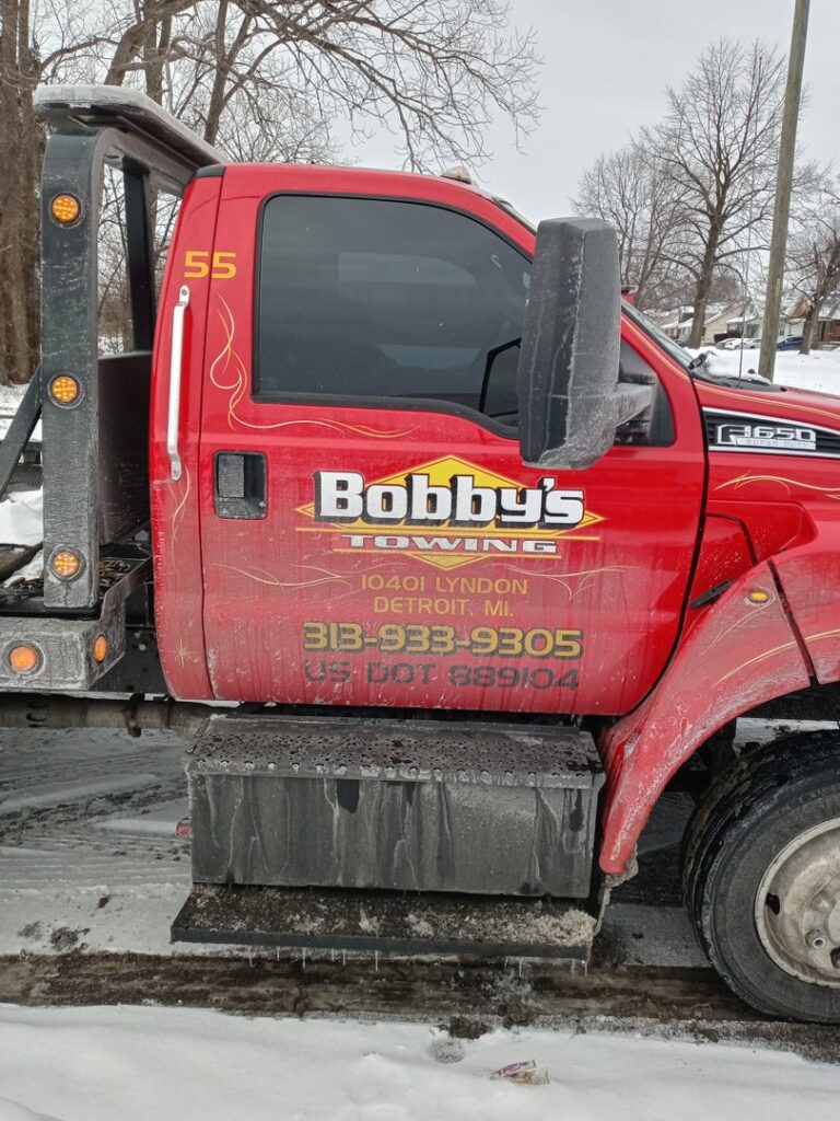 Side view of a red tow truck from Bobby's TCB Towing, covered in ice and snow in Detroit, MI