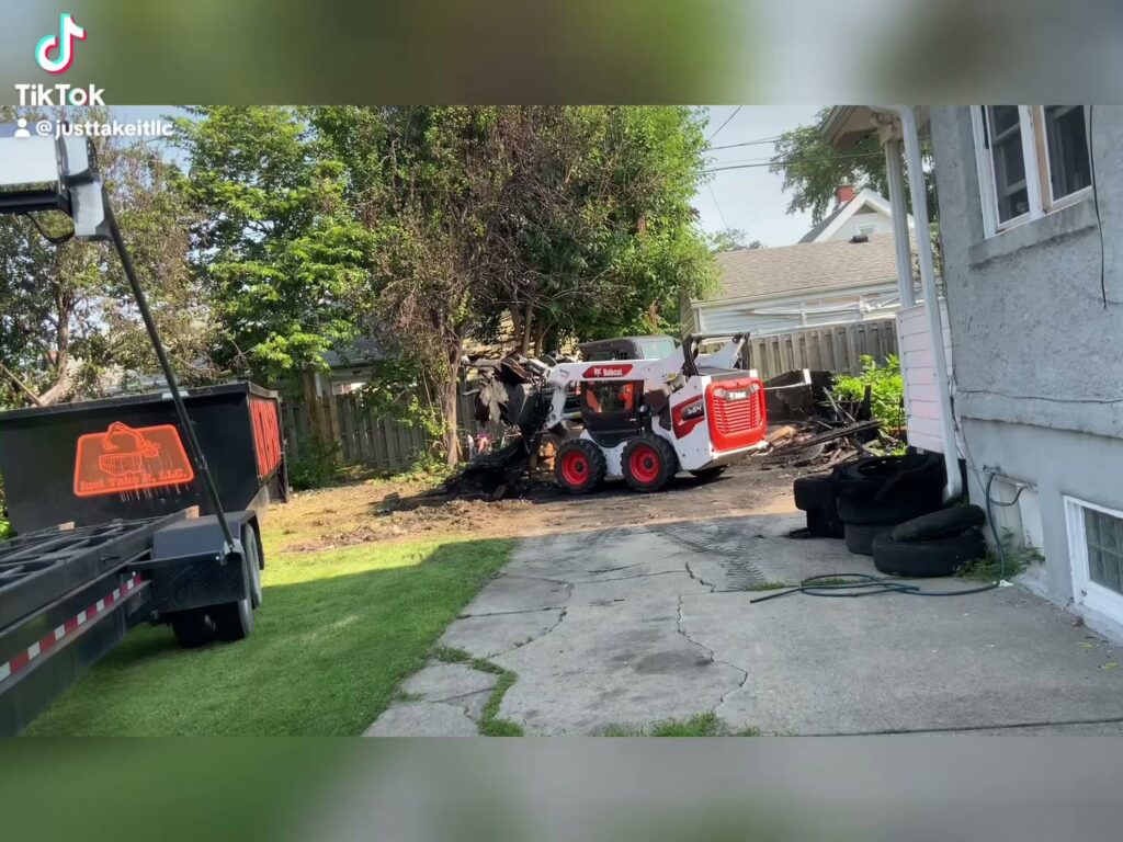 A Bobcat skid-steer loader from Just Take It, LLC. moving demolition debris into a large dumpster trailer in Yorba Linda, CA.
