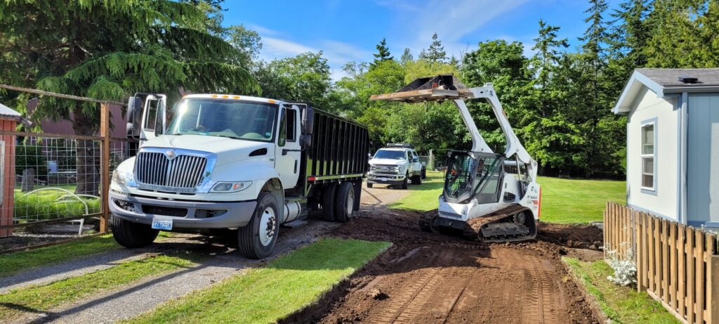 A Bobcat compact track loader loading dirt and debris into a dump truck for ROUGH 2 READY in Auburn, AL