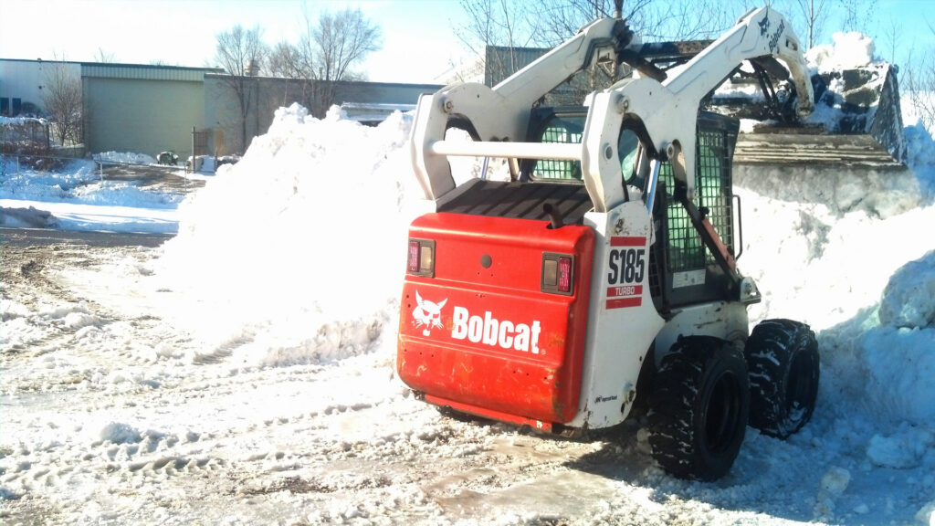 A Bobcat skid-steer loader pushing a large pile of snow, performing snow removal for JC Snow Management in Mount Vernon, NY