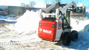 A Bobcat skid-steer loader pushing a large pile of snow, performing snow removal for JC Snow Management in Mount Vernon, NY