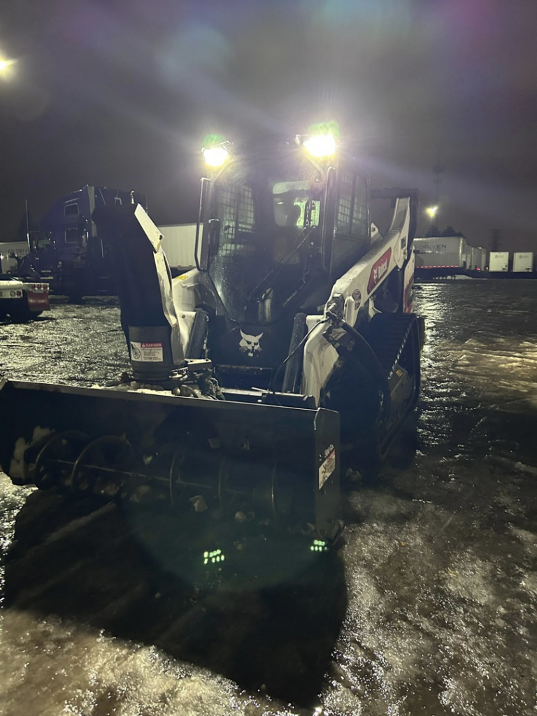 A Bobcat skid steer with a snow blower attachment ready for snow removal at night by Cities Lawn and Snow LLC in Woodbury, MN.