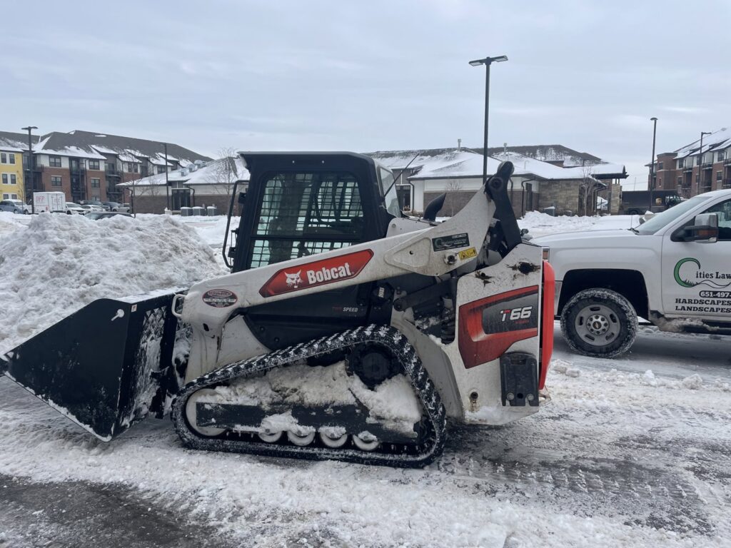 A Bobcat skid steer, essential snow removal equipment, parked in a snowy lot next to a Cities Lawn and Snow LLC truck in Woodbury, MN.
